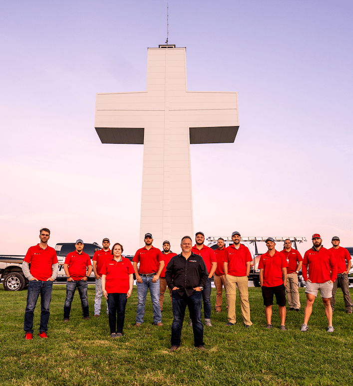 Integrity Roofing & Exteriors team standing together in front of a large cross monument